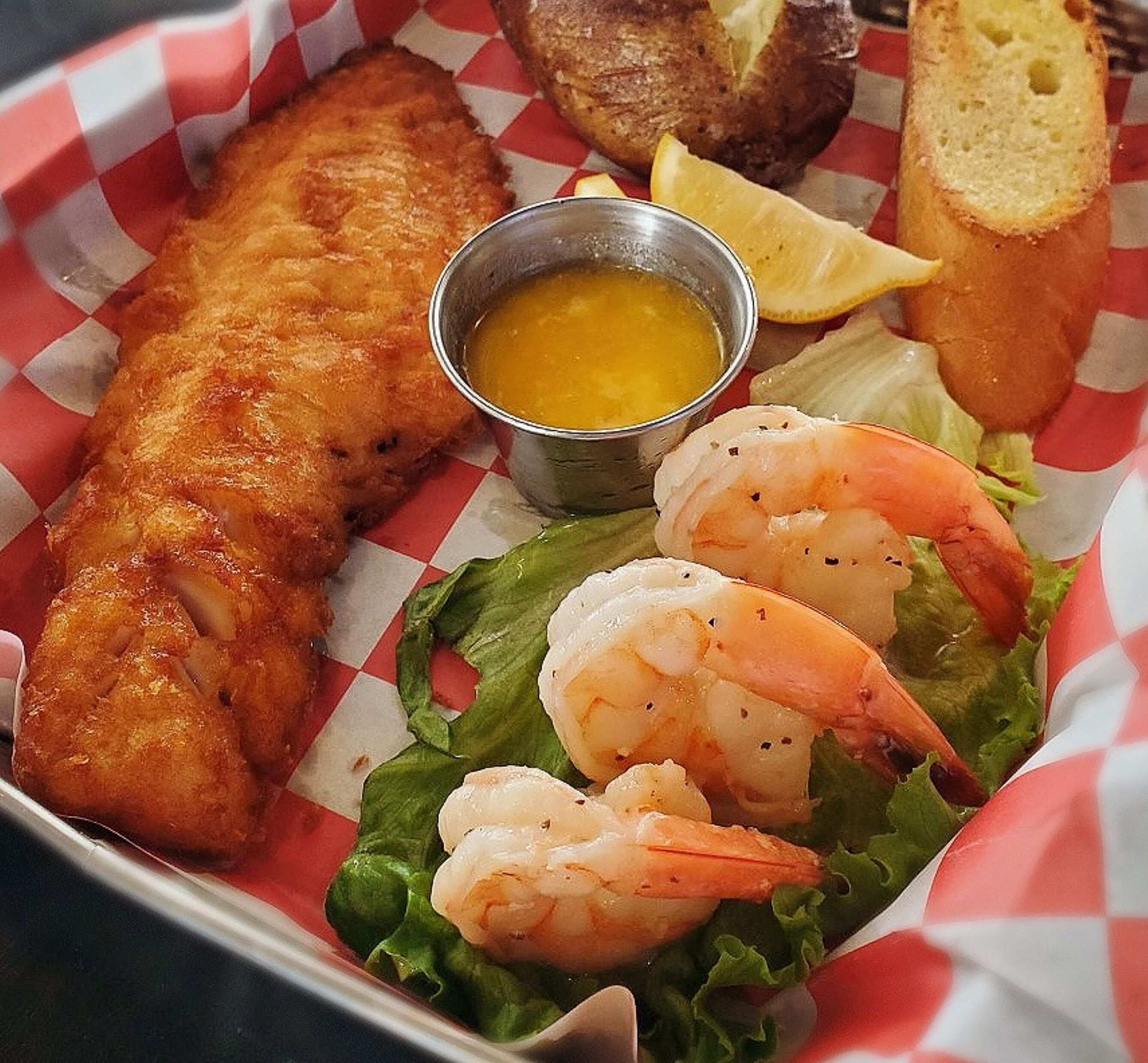 Un repas composé de poisson-frites, de crevettes, d’un petit bol de sauce et d’une tranche de pain.