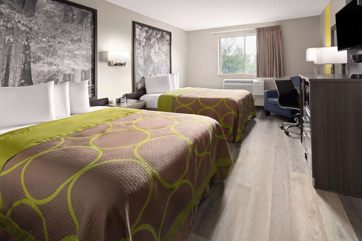 Ein Hotelzimmer mit zwei Betten, einem Schreibtisch, einem Stuhl, einem Fernseher und einem großen Fenster.