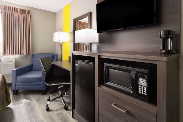 A hotel room with a desk, chair, TV, microwave, and coffee maker.