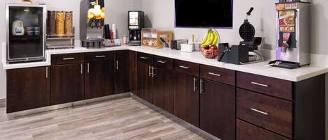 A modern kitchen with a refrigerator, coffee machine, waffle maker, and a flat-screen TV mounted on the wall.