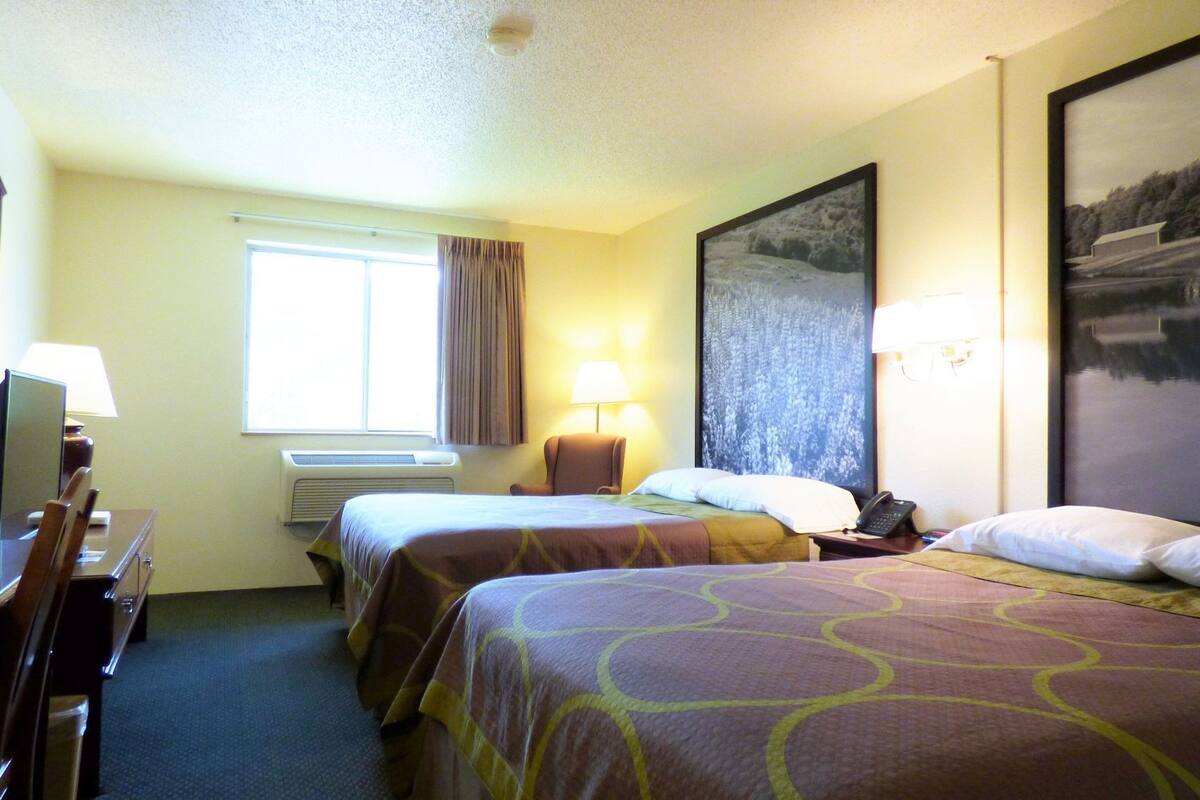 Ein Hotelzimmer mit zwei Betten, einem Schreibtisch, einer Lampe, einem Telefon und einem großen gerahmten Bild an der Wand.