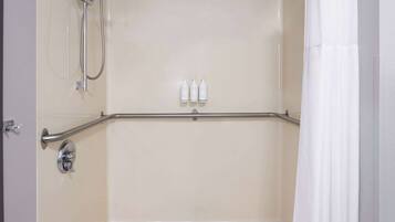 Un espace douche équipé d’une barre d’appui, d’un pommeau de douche et de trois bouteilles de shampoing.