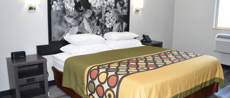A hotel room with a bed, a nightstand, a wall-mounted phone, and a large framed picture.