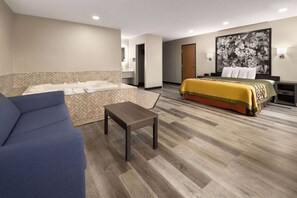 A hotel room with a bed, a sofa, a small table, a bathroom with a bathtub, and a large painting on the wall.