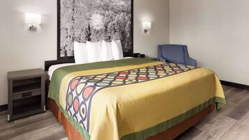 Una habitación de hotel con una cama grande, una silla, una mesita de noche y una lámpara de pared.