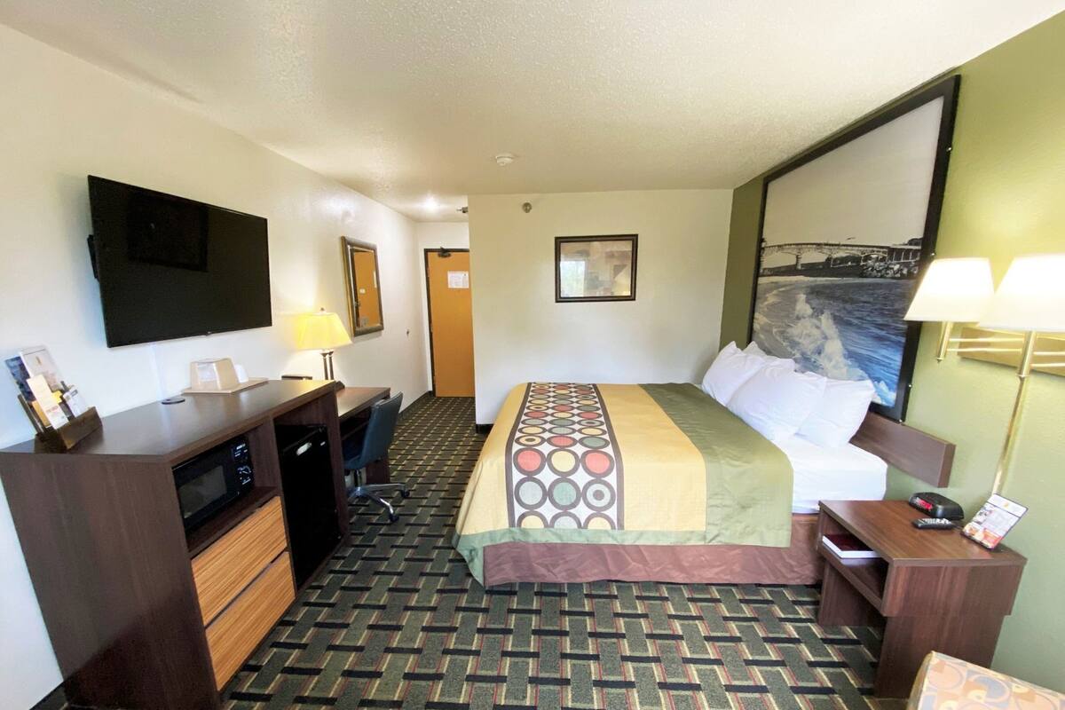 A hotel room with a bed, desk, chair, and a television.