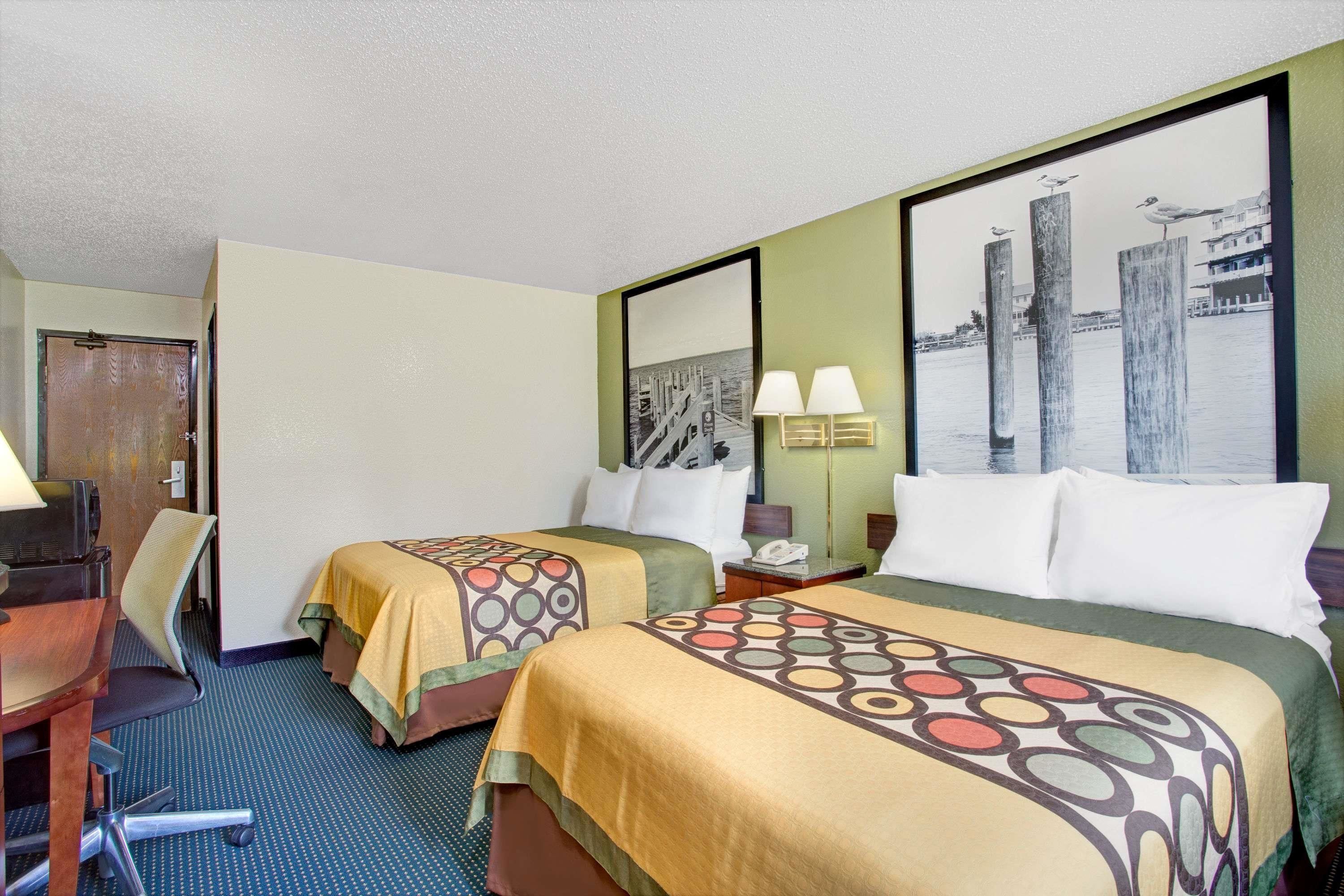 Een hotelkamer met twee bedden, een bureau, een stoel en een groot raam met uitzicht op de stad.