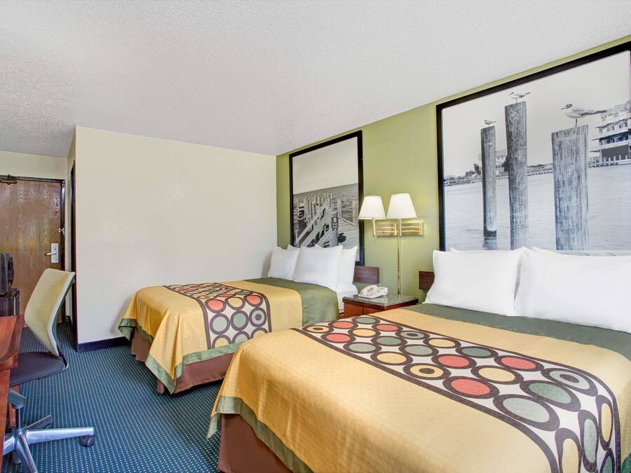 Een hotelkamer met twee bedden, een bureau, een stoel en een groot raam met uitzicht op de stad.
