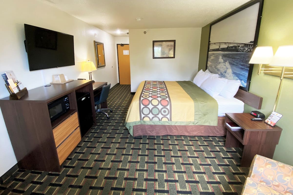 A hotel room with a bed, desk, chair, and a TV on the wall.