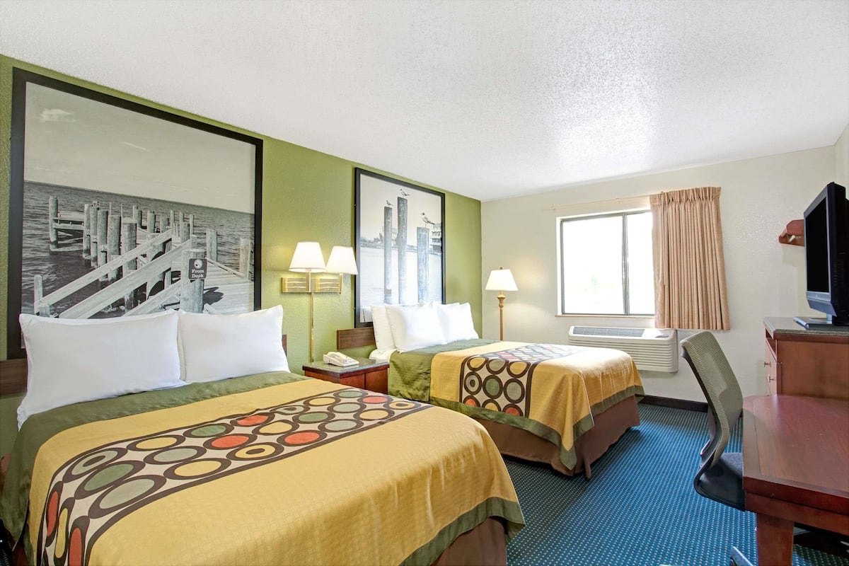A hotel room with two beds, a desk, a chair, a television, and a window with curtains.