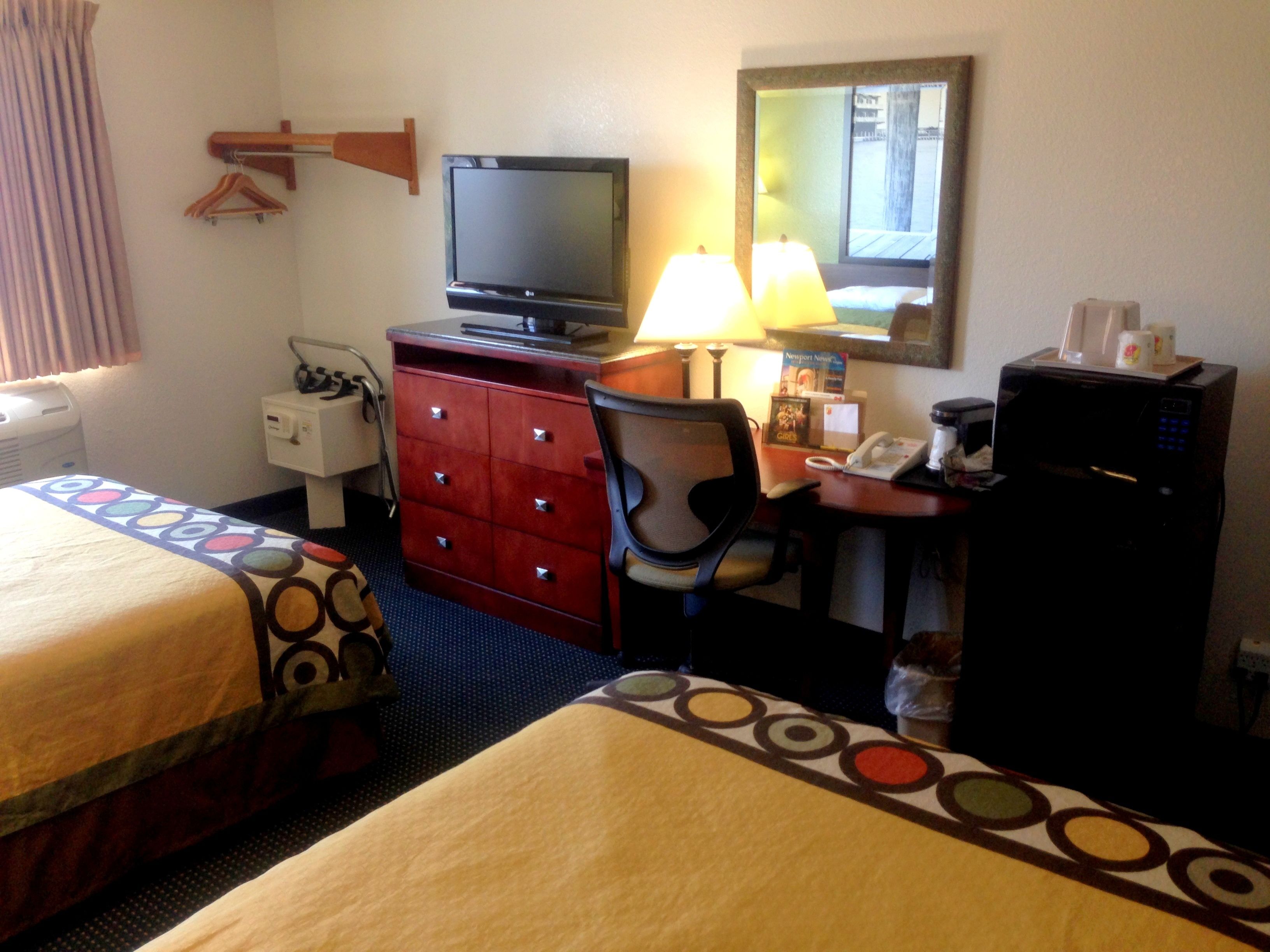 Ein Hotelzimmer mit zwei Betten, einem Schreibtisch mit Computer, einem Fernseher, einem Spiegel und einem Kühlschrank.