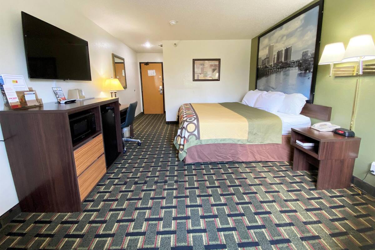 A hotel room with a bed, desk, chair, and a TV.