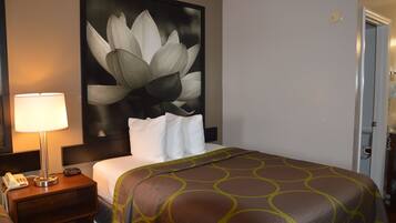 A hotel room with a large bed, a nightstand with a lamp, a telephone, and a wall-mounted artwork of a flower.