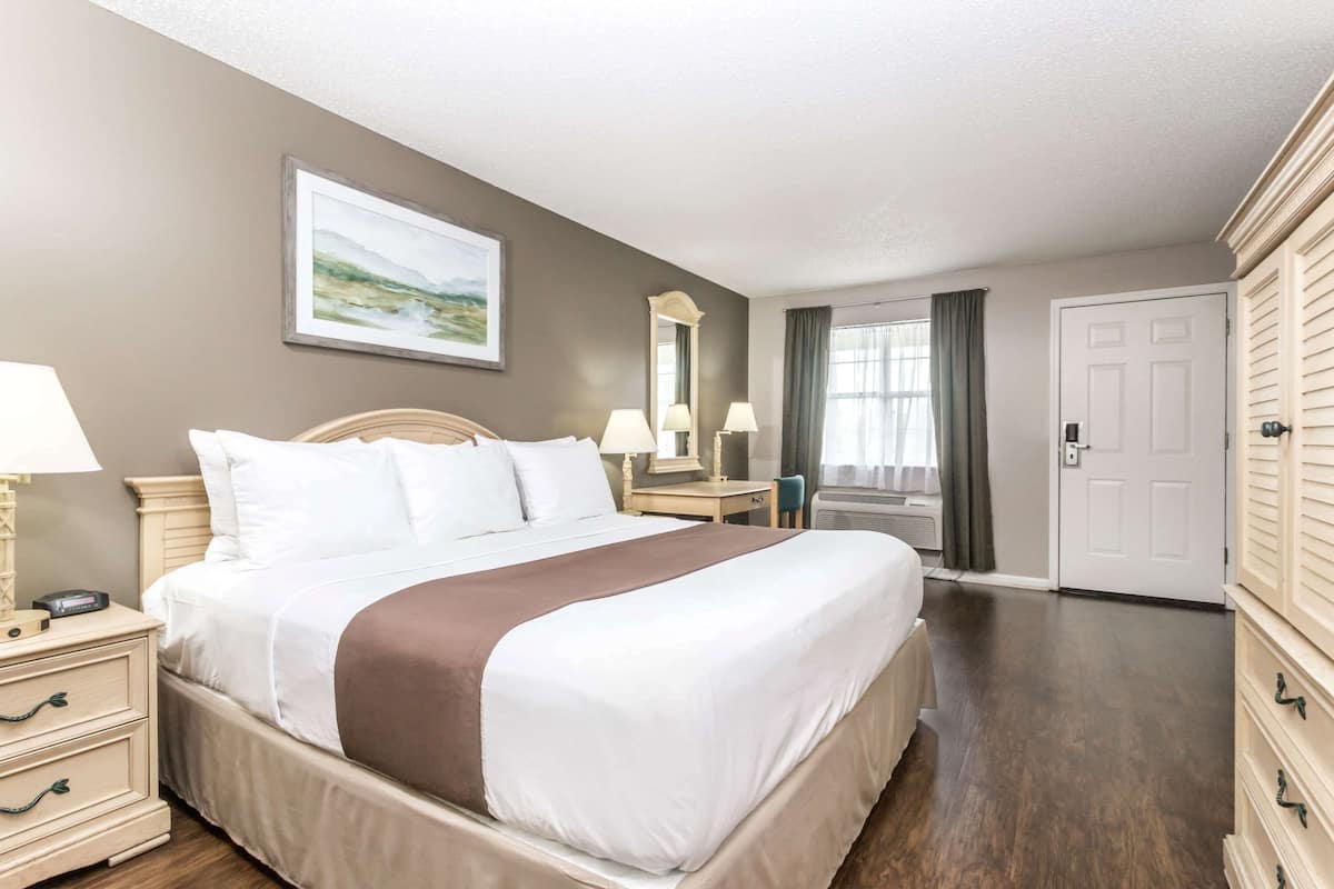 A neatly arranged hotel room with a large bed, bedside tables, a dresser, and a window with curtains.
