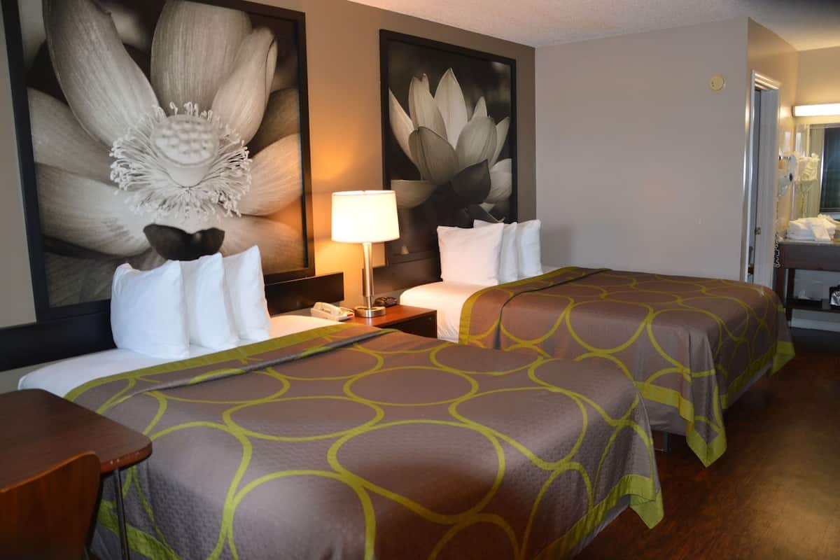 A hotel room with two beds, a nightstand, a lamp, and large floral wall art.
