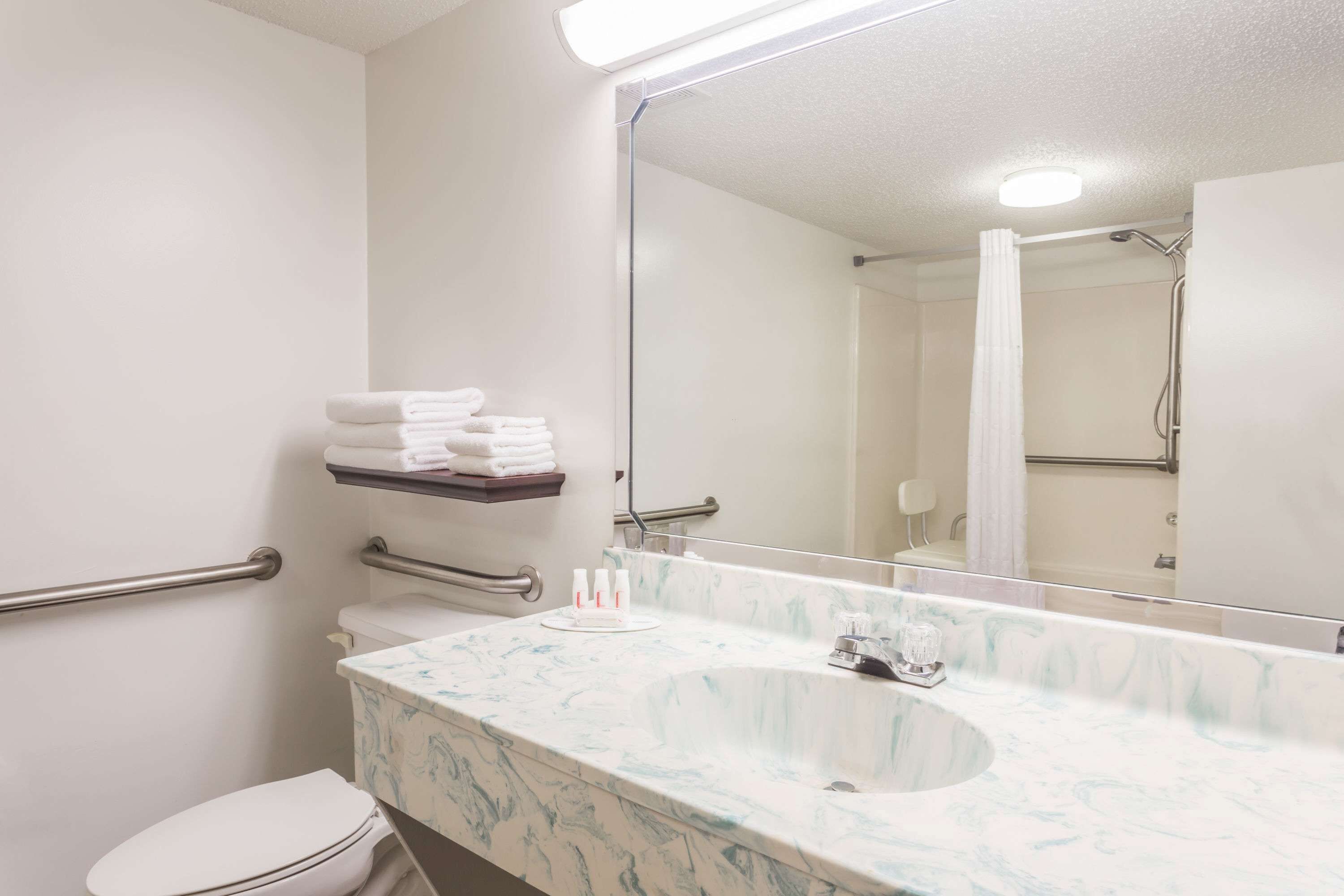 Un baño con lavamanos de mármol, inodoro, espejo y zona de ducha.
