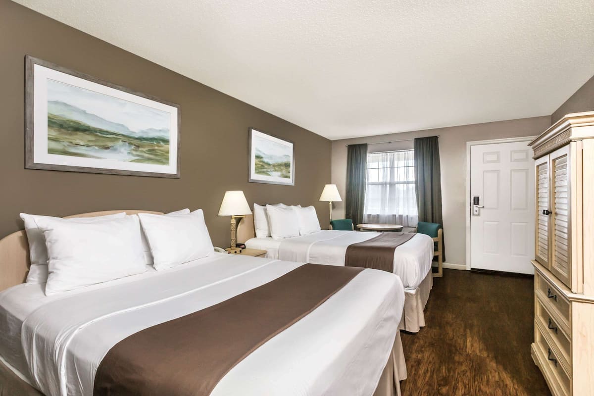 A hotel room with two beds, a dresser, and two framed landscape paintings on the wall.