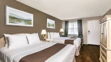 A hotel room with two beds, a dresser, and two framed landscape paintings on the wall.