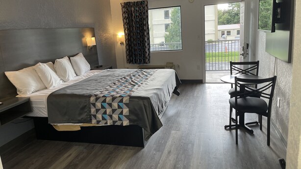 A modern hotel room with a large bed, a desk, and a balcony with a view of the outside.