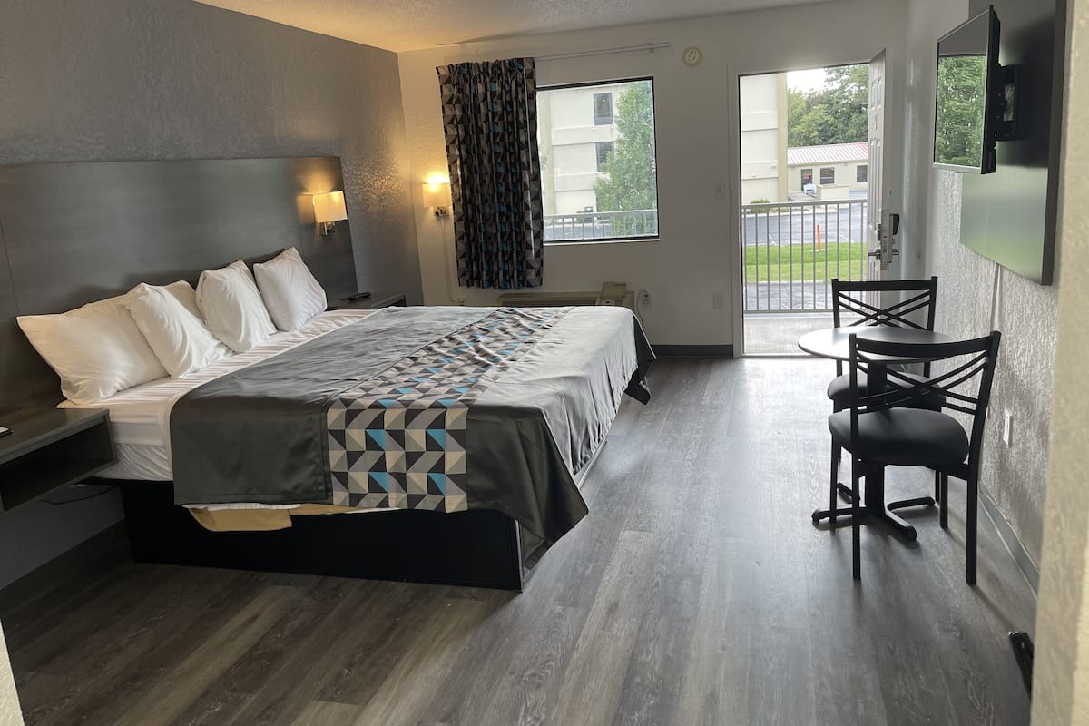 A modern hotel room with a large bed, a desk, and a balcony with a view of the outside.