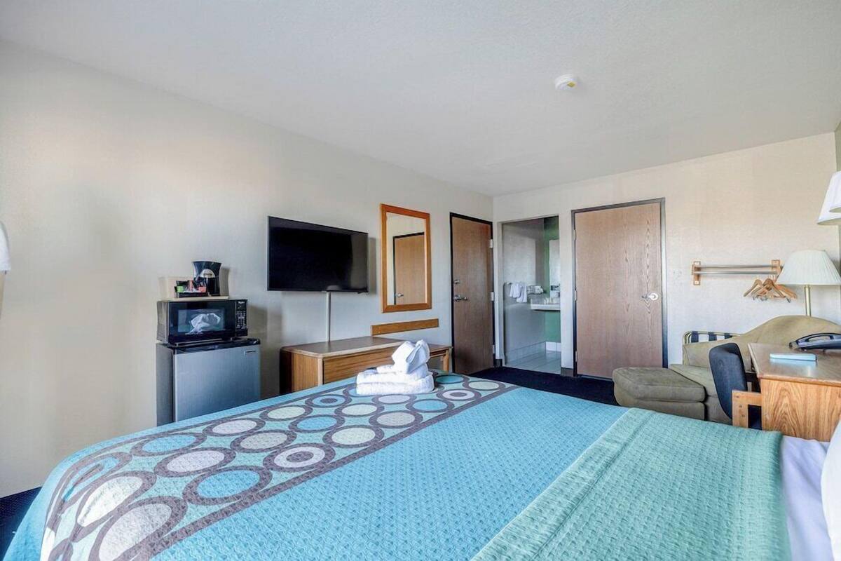 Une chambre d’hôtel équipée d’un lit, d’un bureau, d’une télévision, d’un miroir, d’une armoire et d’une porte de salle de bain.