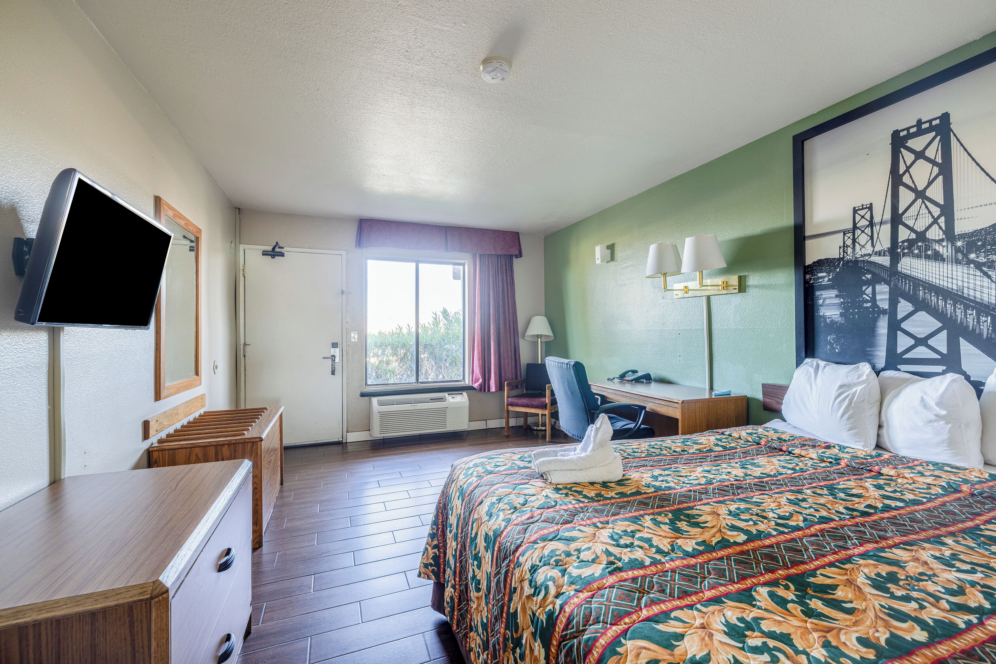 A hotel room with a bed, a desk, a chair, a television, and a window with curtains.