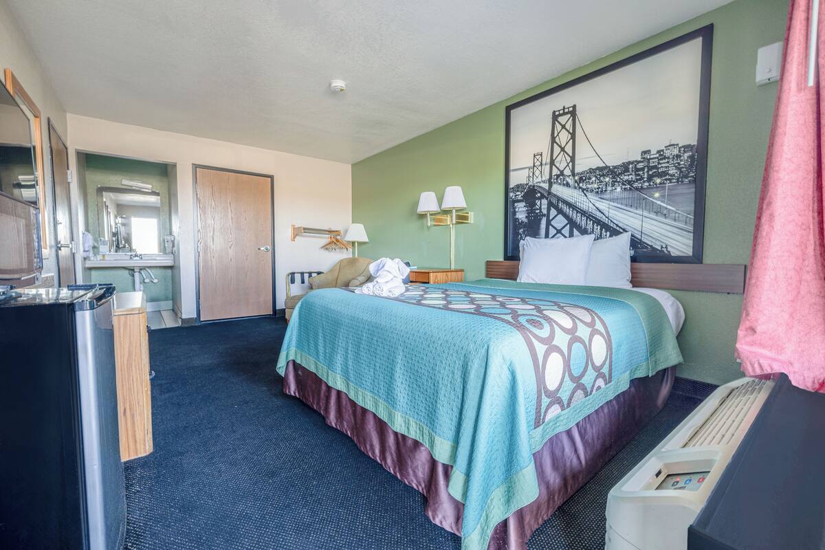 Une chambre d’hôtel avec un lit, un bureau, un miroir, une lampe et un tableau représentant un pont.