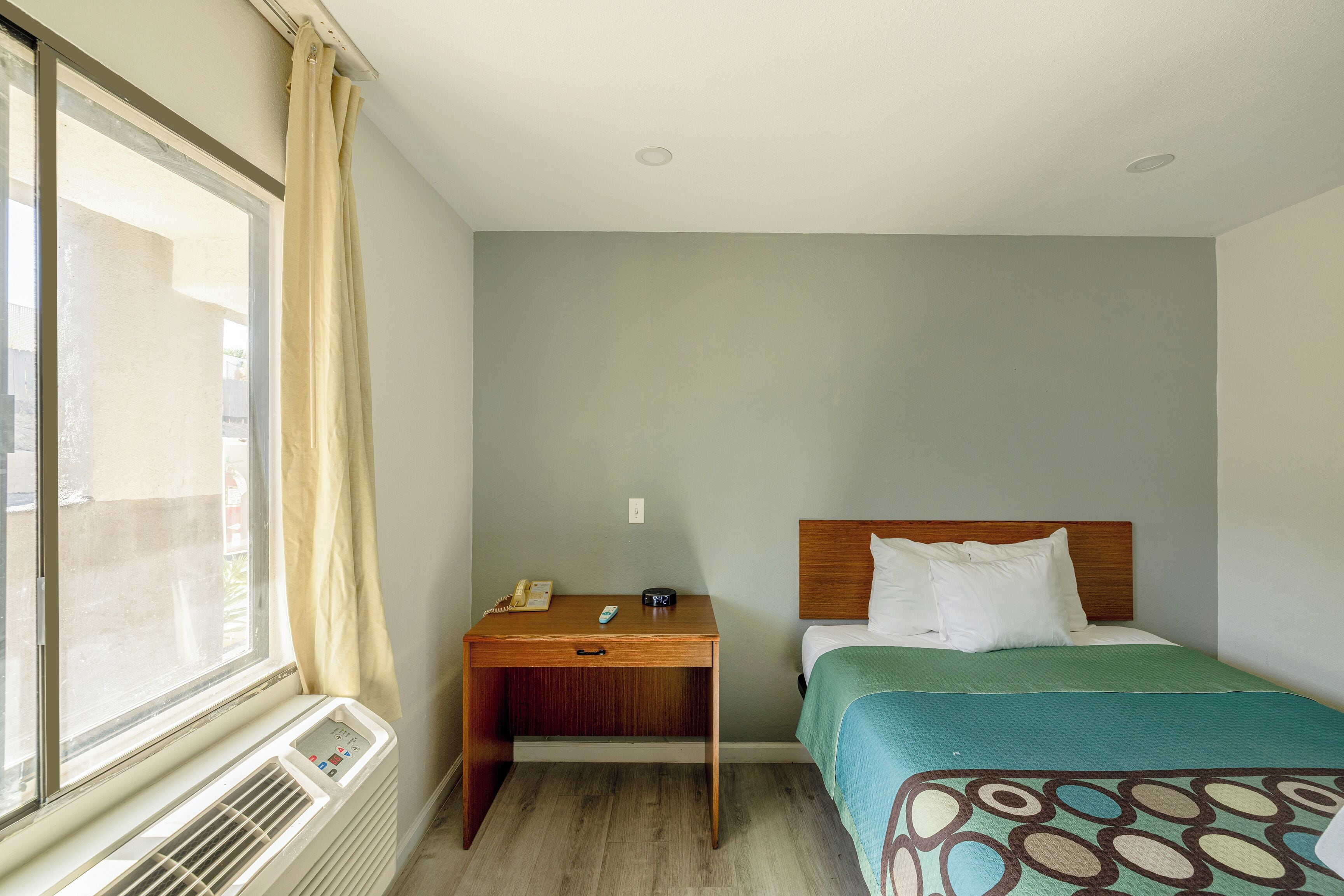 Una habitación de hotel con cama, mesita de noche y ventana con cortinas.