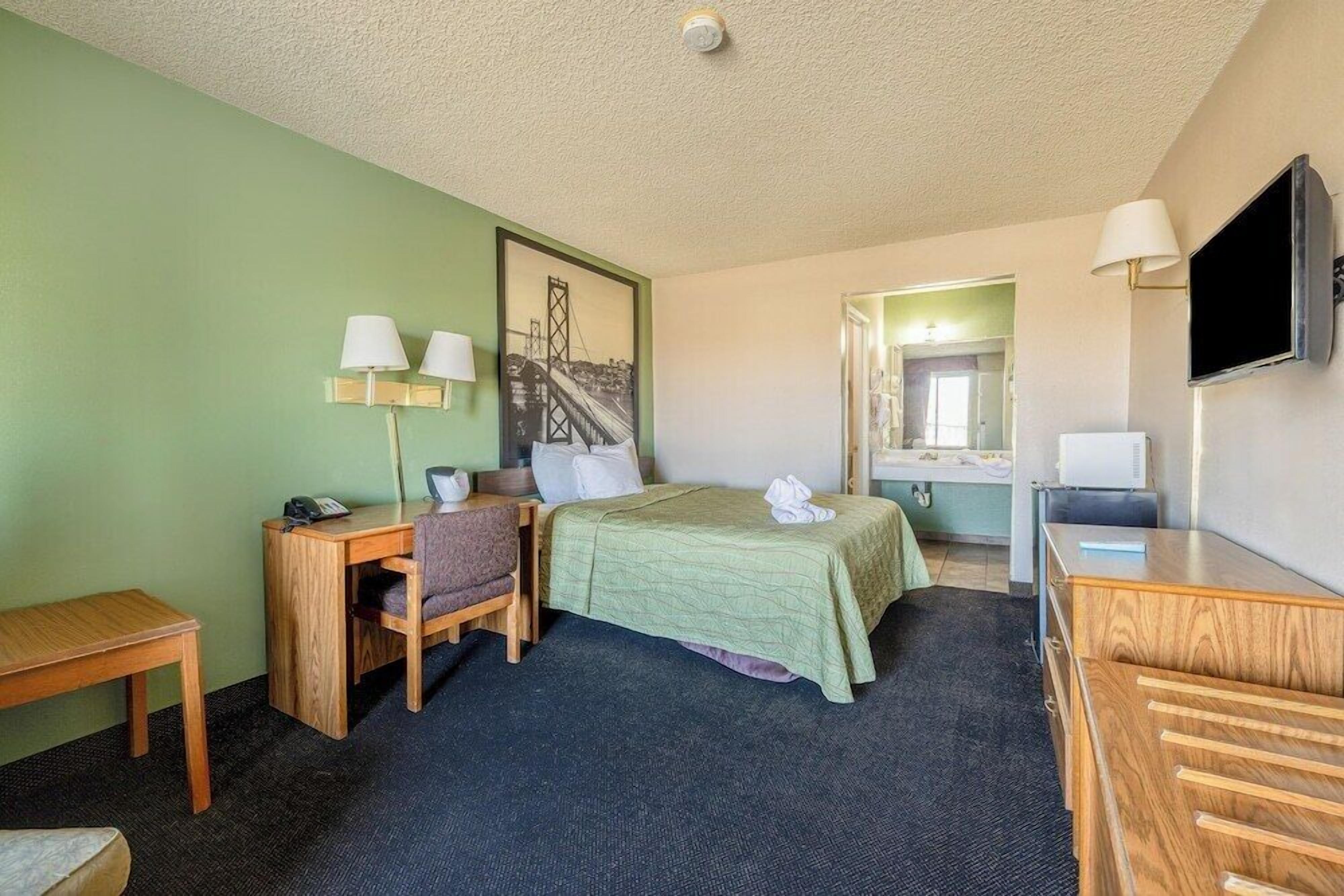 A hotel room with a bed, desk, chair, and a television.