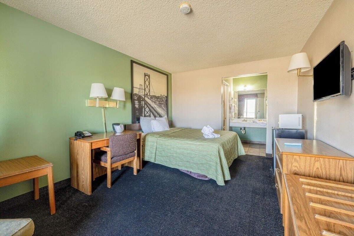 A hotel room with a bed, desk, chair, and a television.