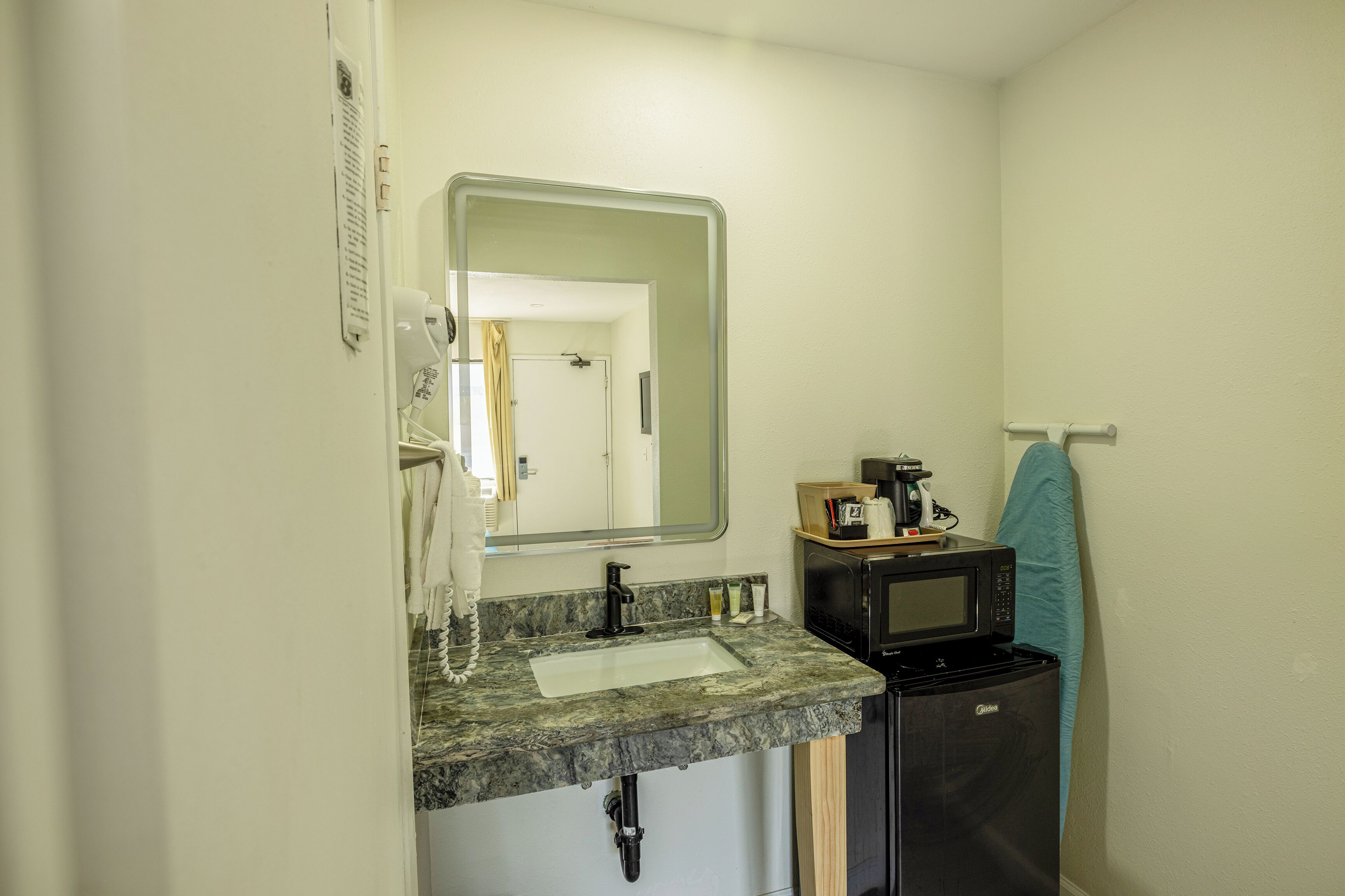 Un baño pequeño con lavamanos, espejo y microondas.