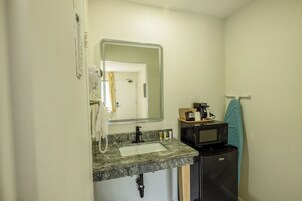 Un baño pequeño con lavamanos, espejo y microondas.