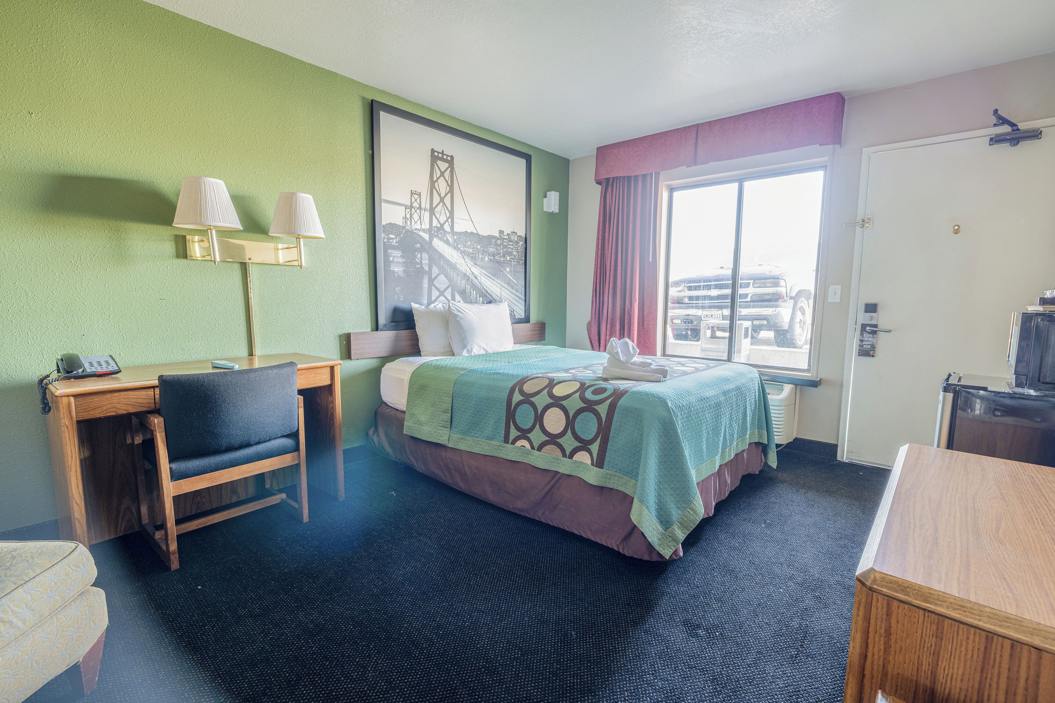 Habitación de hotel con cama, escritorio, silla y un ventanal amplio.