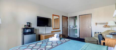 Habitación de hotel con cama, escritorio, silla, televisor, microondas y baño visible a través de una puerta abierta.