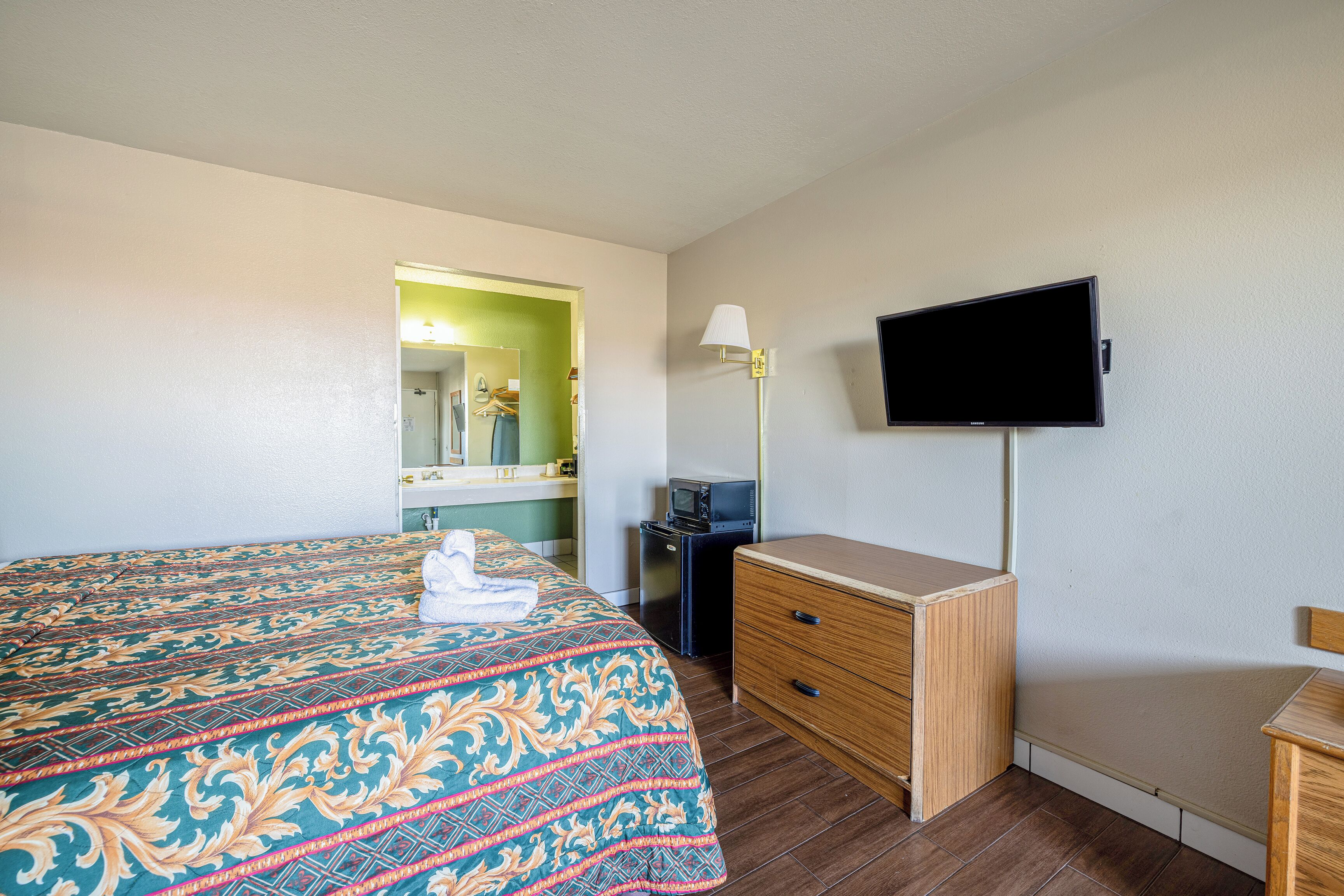 Une chambre d’hôtel avec un lit, une commode, une télévision et un miroir.