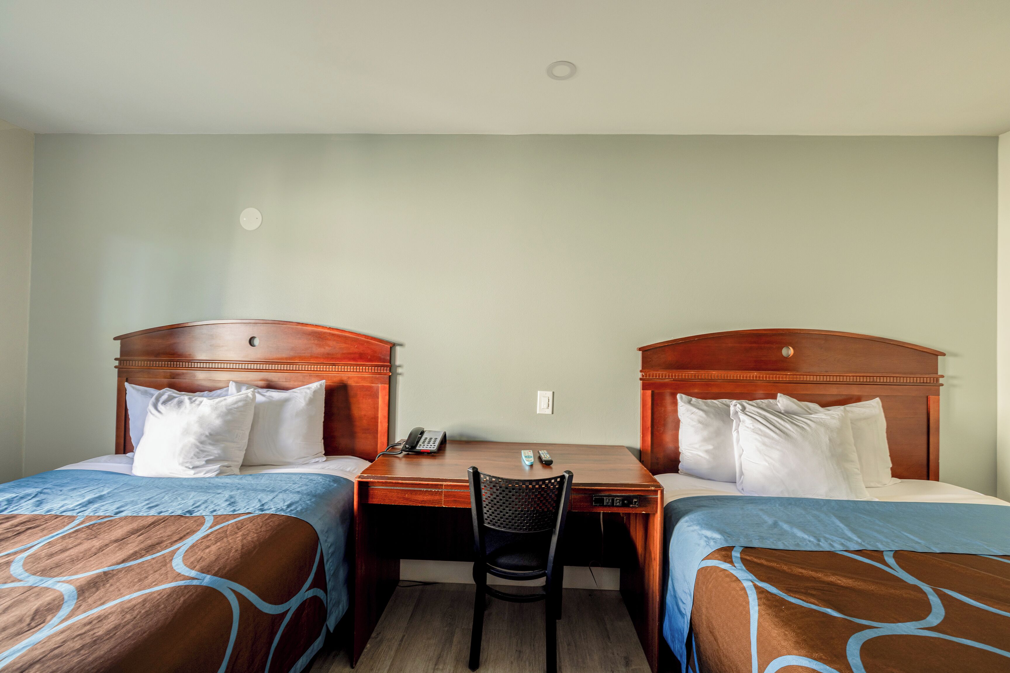 A hotel room with two single beds, a desk, and a chair.