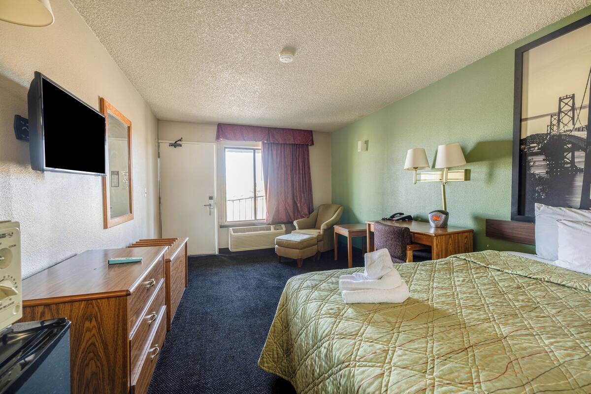 Une chambre d’hôtel équipée d’un lit, d’un bureau, d’une chaise, d’une télévision et d’une fenêtre avec des rideaux.
