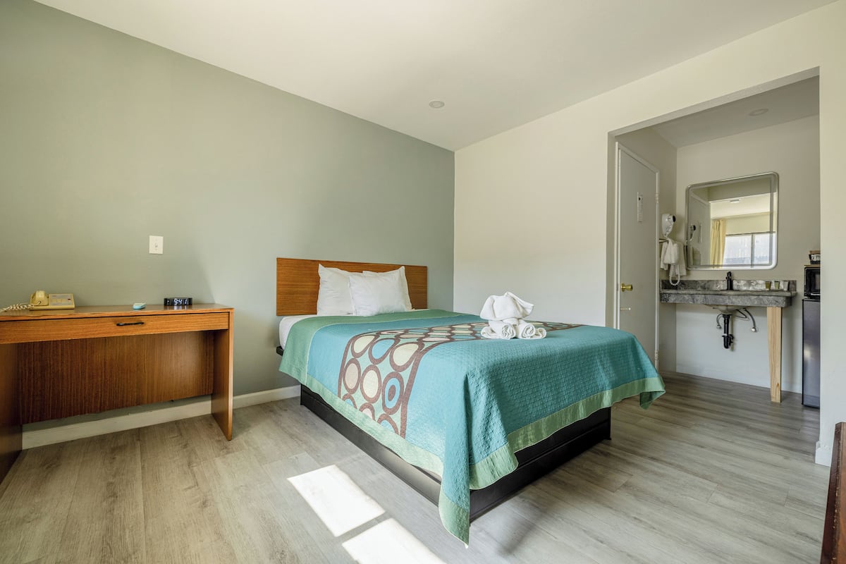 Une chambre à coucher avec un lit, un bureau en bois et une salle de bain avec un lavabo et un miroir.