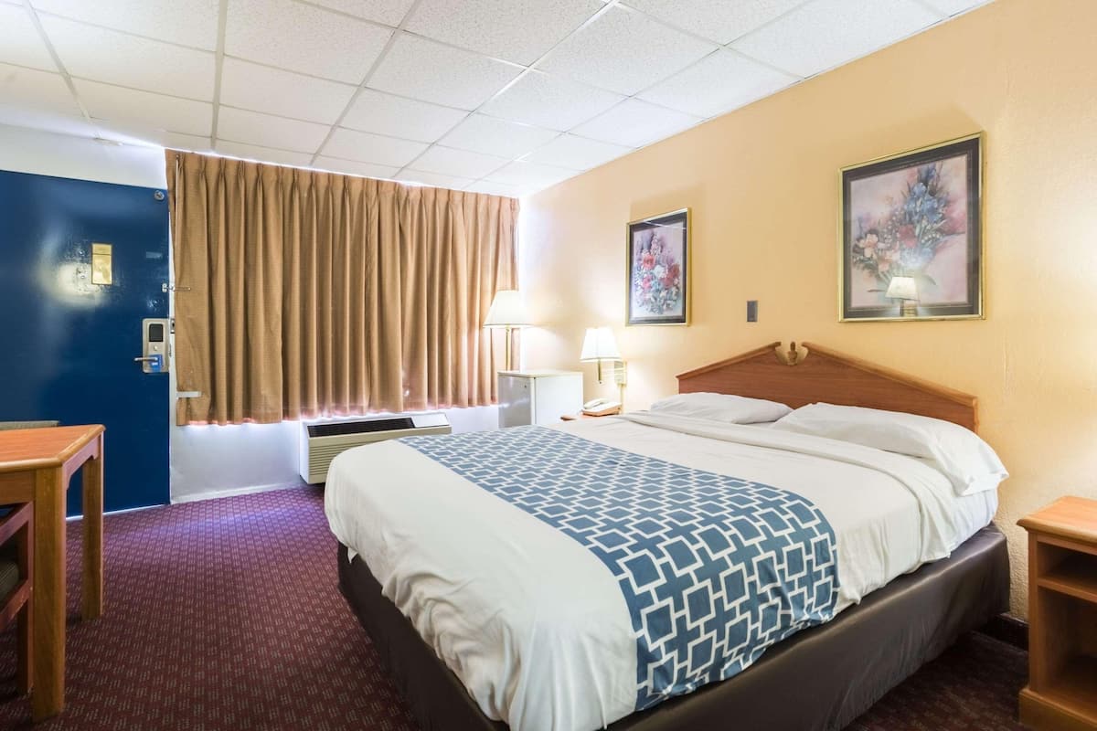 A hotel room with a bed, bedside tables, a desk, a lamp, and two framed pictures on the wall.