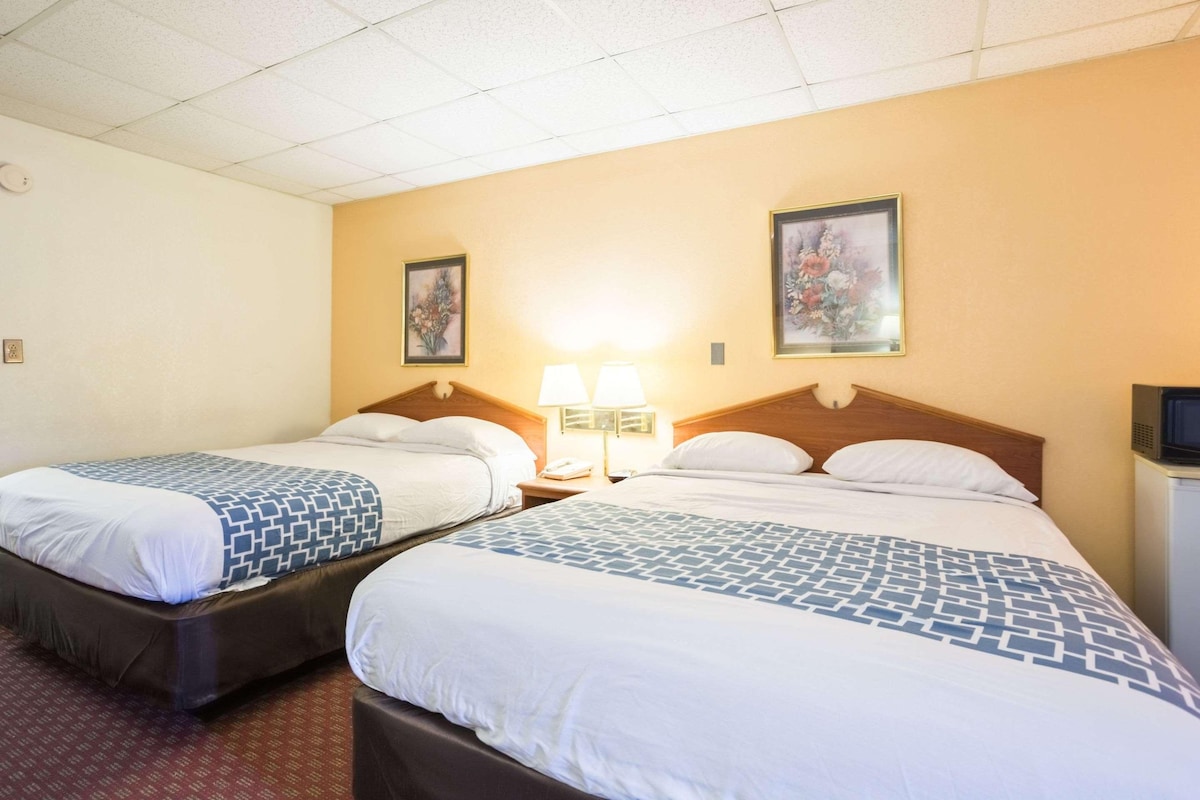 A hotel room with two beds, a nightstand with a lamp, and a television on a small cabinet.