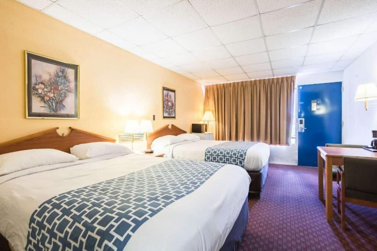 A hotel room with two beds, a desk, a chair, and a door.