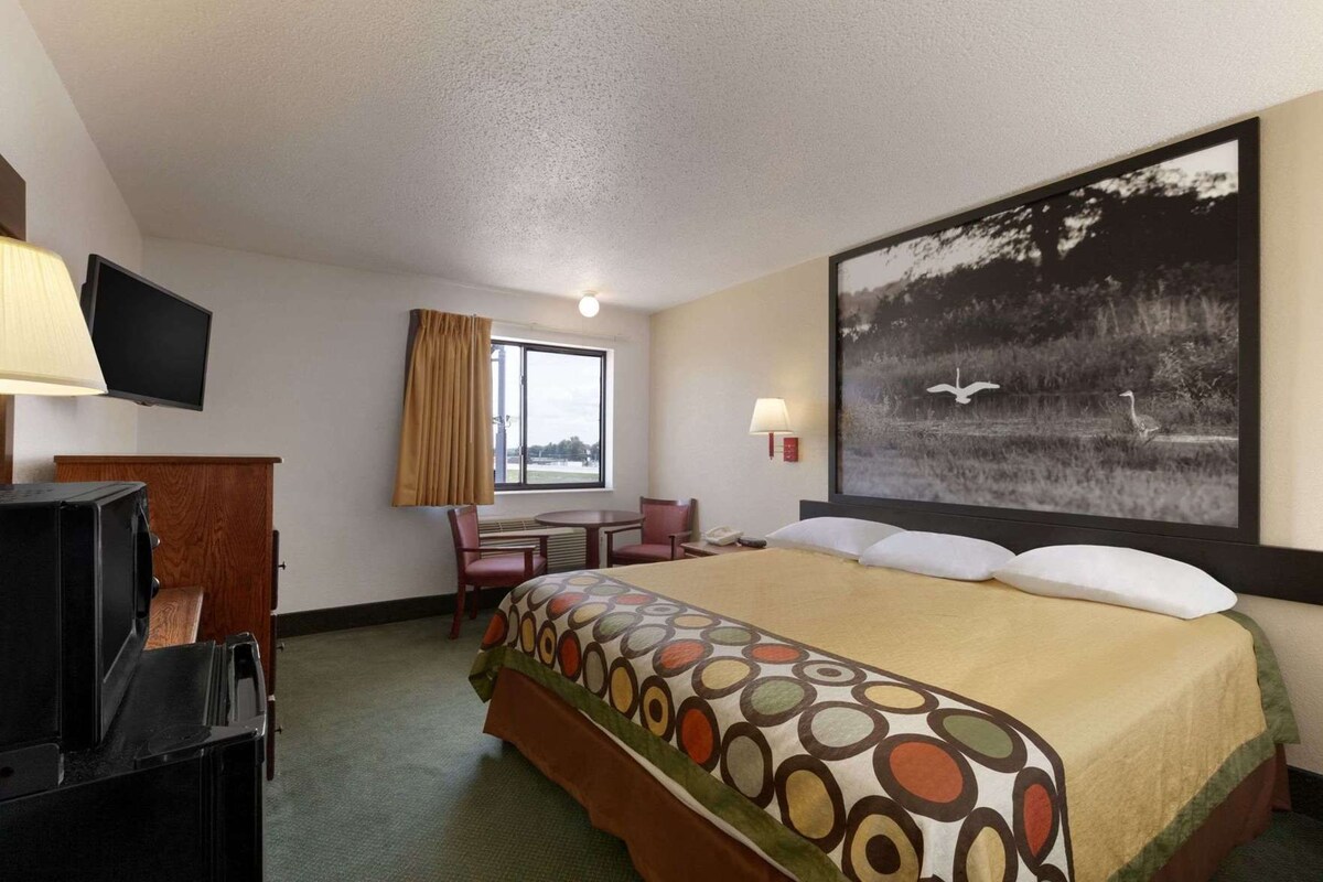 Ein Hotelzimmer mit einem Bett, einem Schreibtisch, einem Sessel, einem Fernseher und einem großen Fenster.