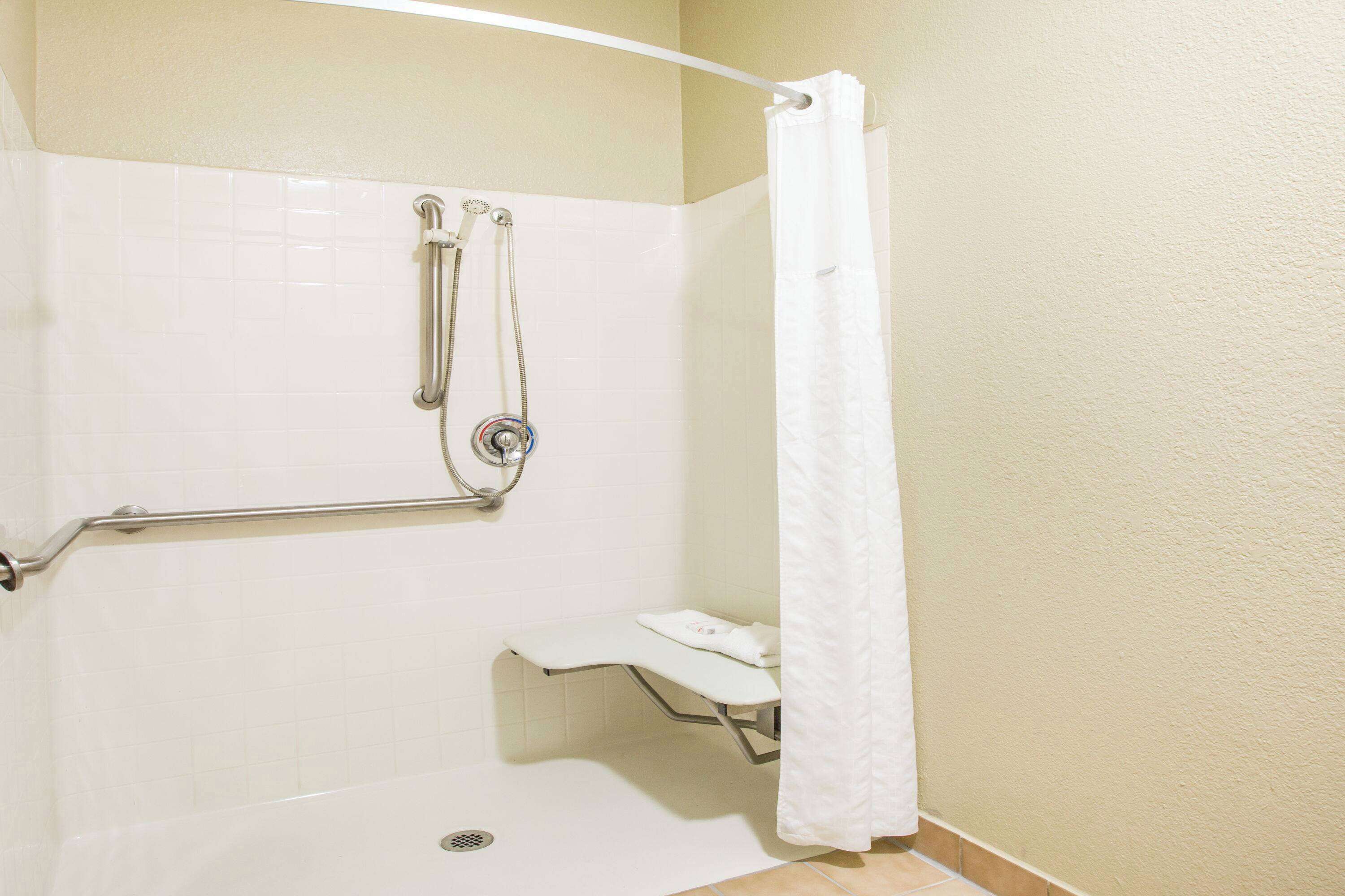 A bathroom with a shower, grab bar, and a bench.