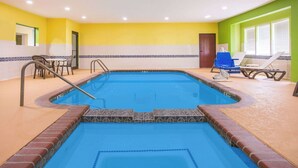 Una piscina interior con una fuente de agua azul, rodeada por una terraza con baldosas y equipada con sillones de descanso y una mesita.