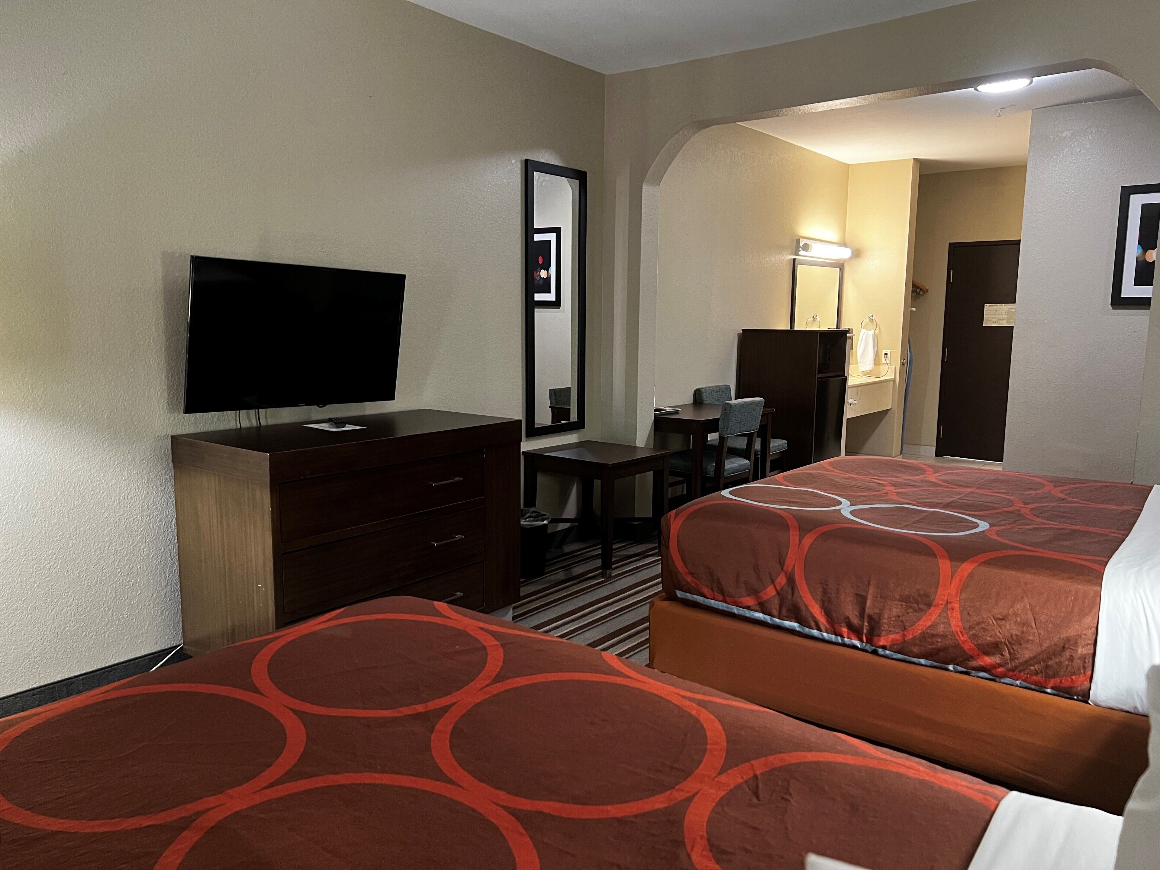 A hotel room with two beds, a desk, a television, and a mirror.