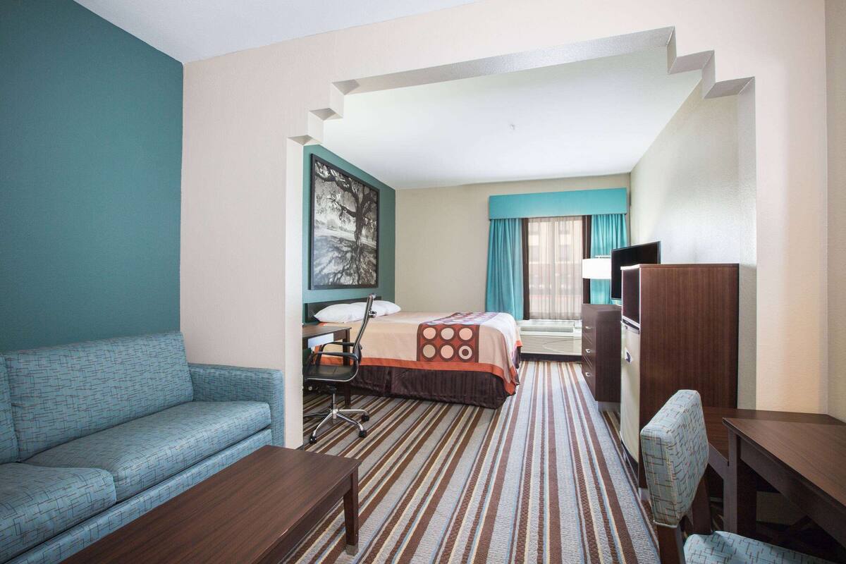 Habitación de hotel con sofá, cama con colcha a rayas, escritorio con silla, televisión y ventana con cortinas.