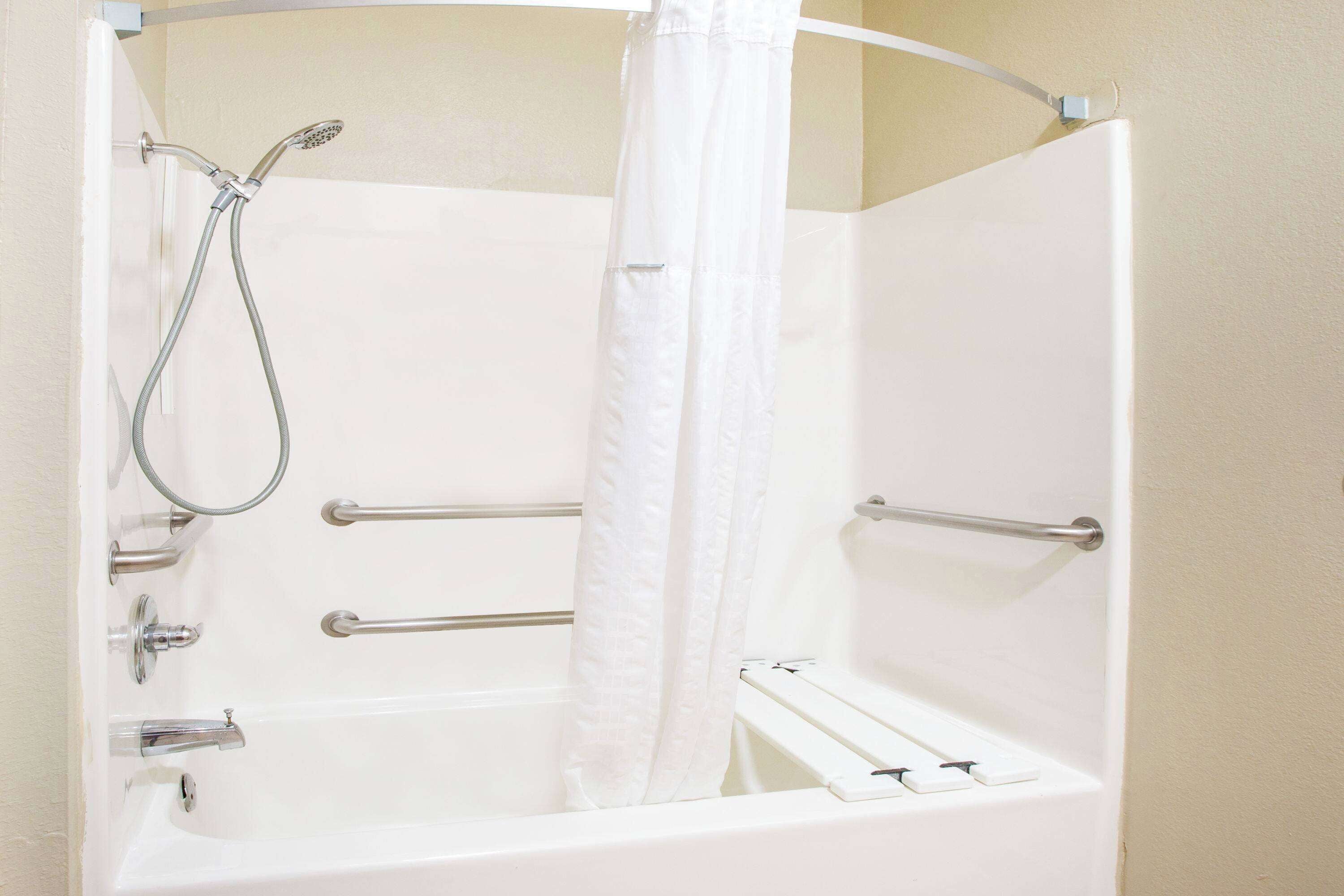 Eine weiße Badewanne mit Duschkopf, Haltegriffen und einem Vorhang.