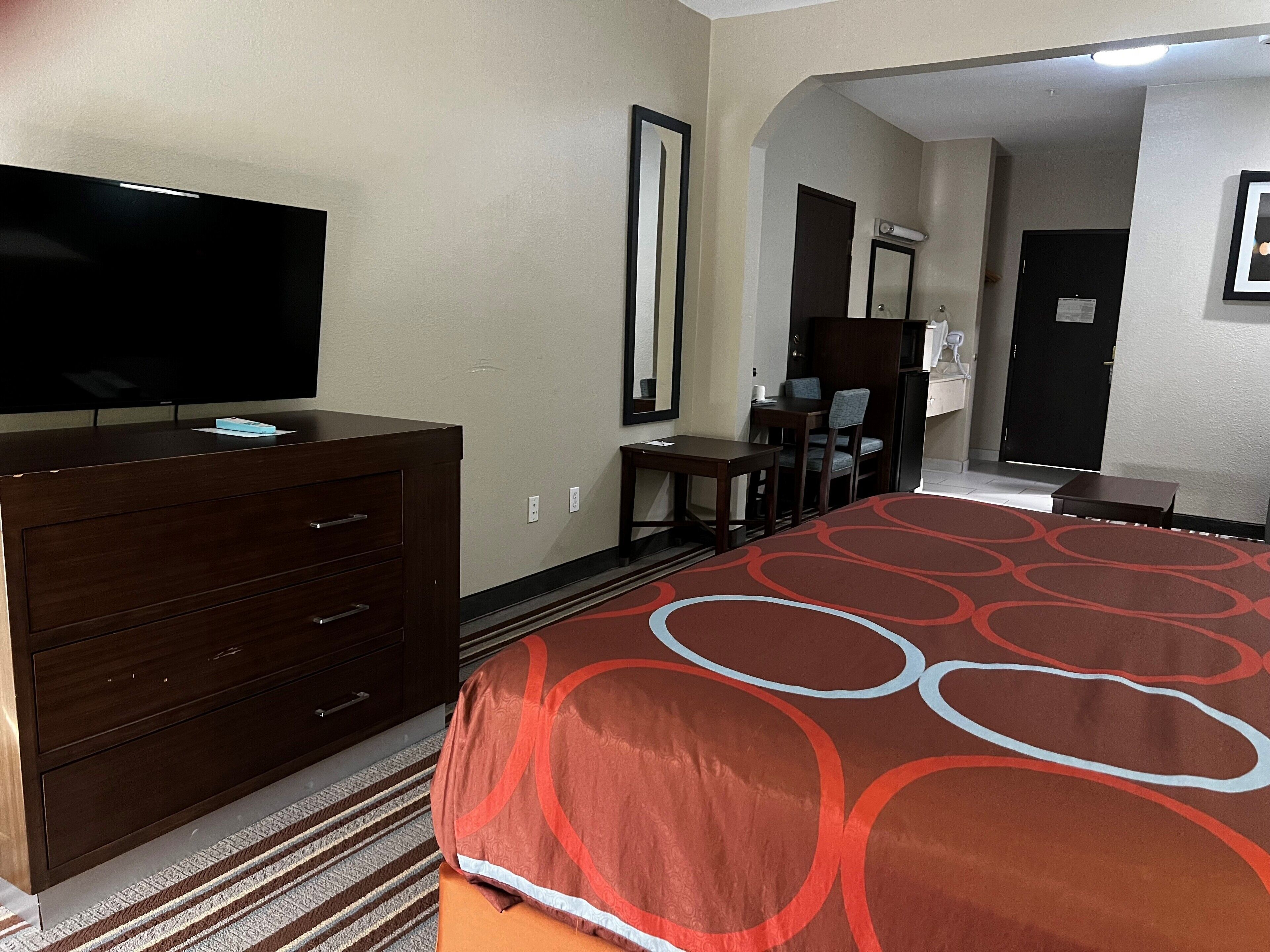 A hotel room with a large bed, a dresser, a television, a desk, and a chair.