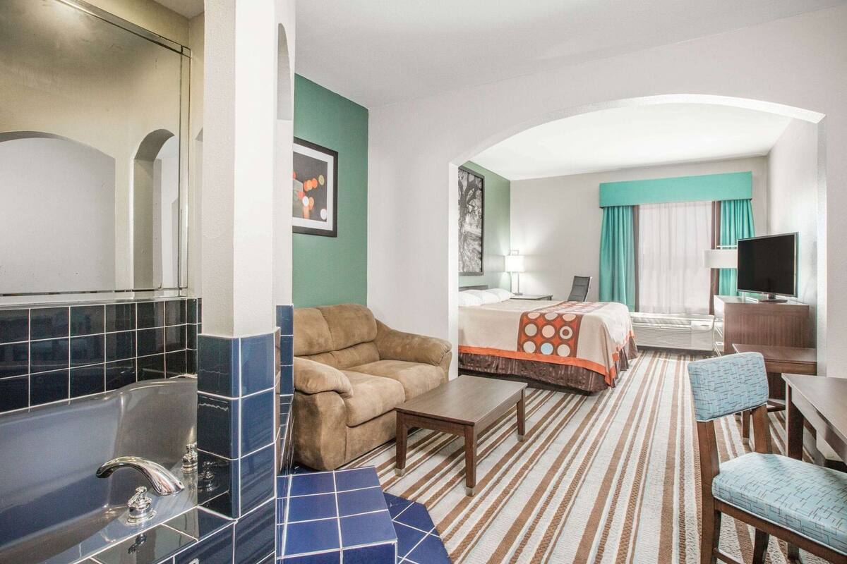 Habitación de hotel con cama, sofá, escritorio, televisor y baño con bañera y lavabo.