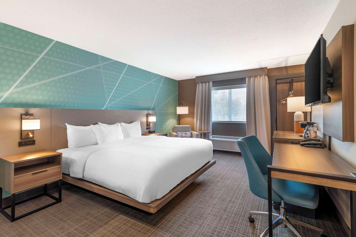 Ein Hotelzimmer mit Bett, Schreibtisch, Stuhl und einem großen Fenster.